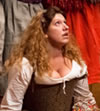 The Jailer's Daughter, in country patterned Elizabethan dress, kneels on the floor looking up in distraction with the legs of the Morris dancers behind her. 