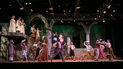 Production photo of Morris dancers twirling handkerchiefs performing for Theseus's royal party watching on the ledge above.