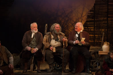 Silence with mug in brown coat, vest, white beard, Falstaff with tankard in right hand, left hand on cane, Shallow with pen and paper in hand, formal red coat, all sitting on a hay waggon, a white ewer to one side, you can see a portion of Bardolph to the left and the page to the right